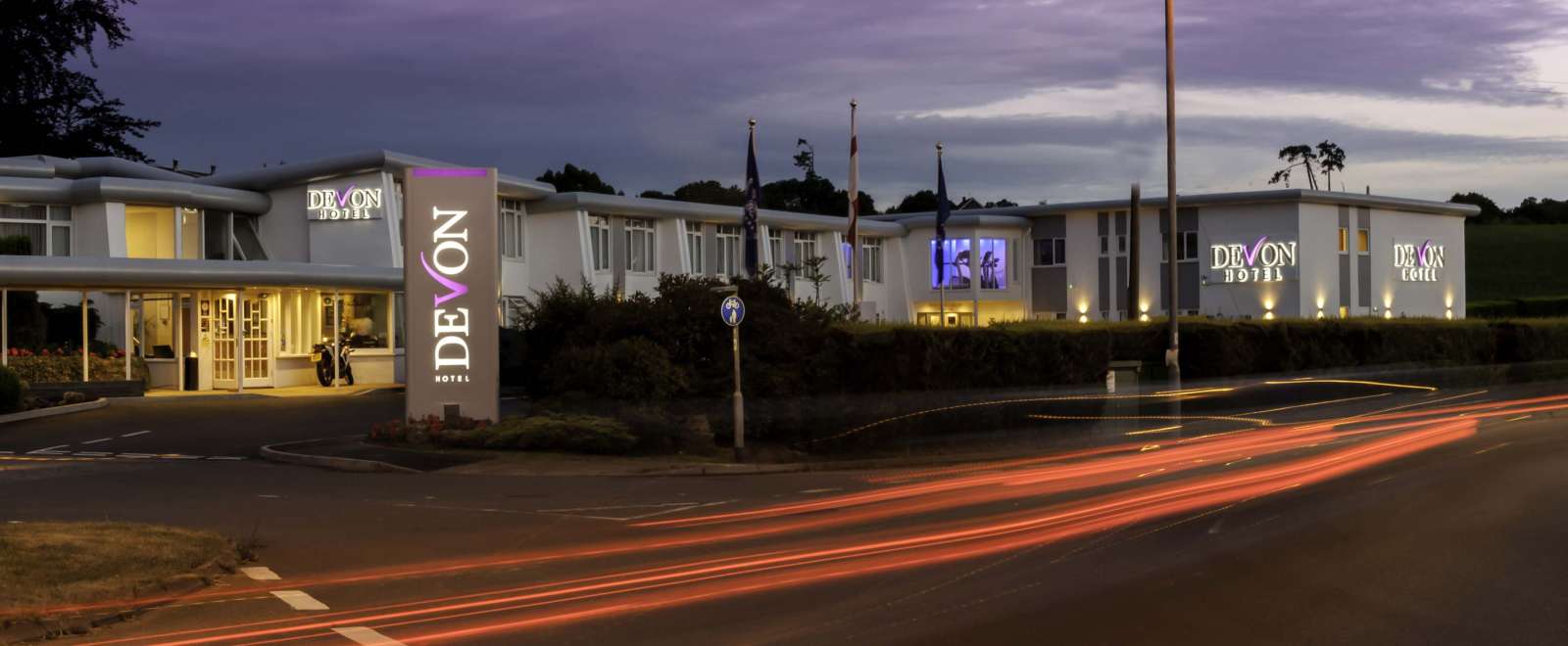 Devon Hotel Exterior with Sign and Flags at Night