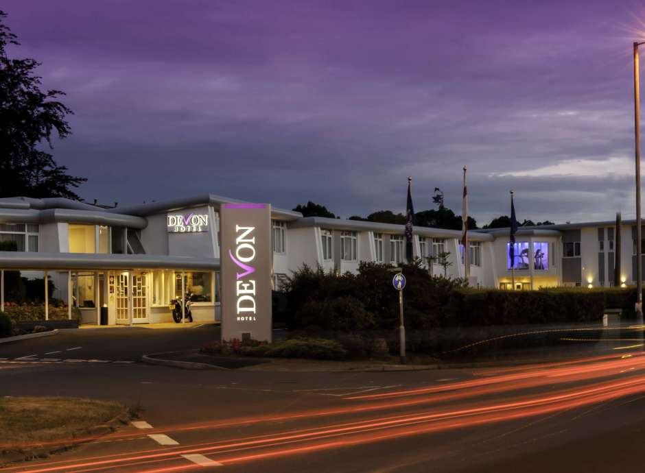 Devon Hotel Exterior with Sign and Flags at Night