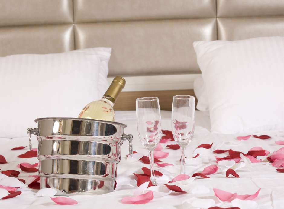 wine and rose petals on bed