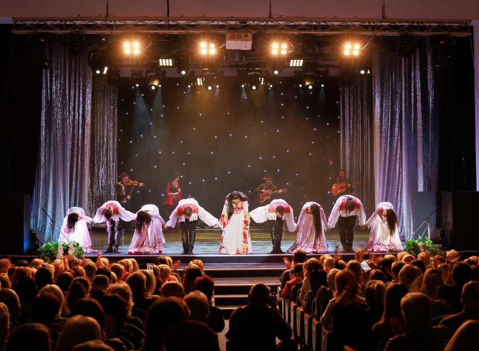 A collective of musicians, singers and dancers in gypsy costumes perform on stage